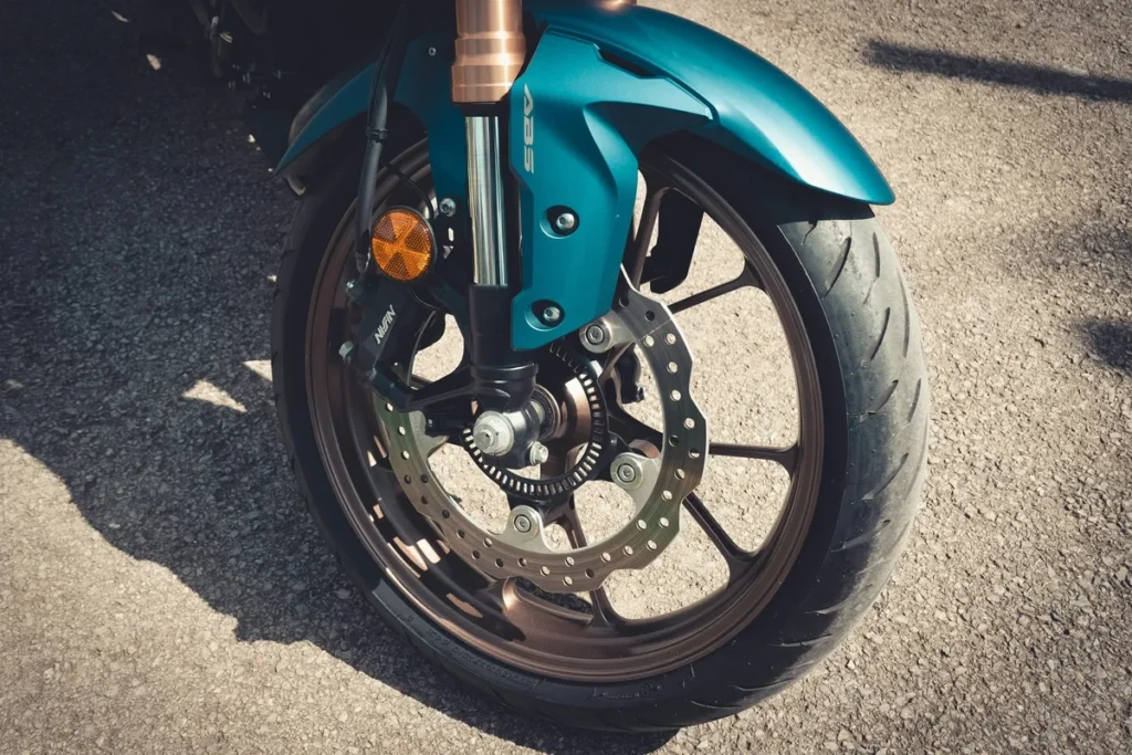Roda dianteira de uma motocicleta com freio a disco ABS, suspensão invertida e pneu esportivo em contato com o asfalto.