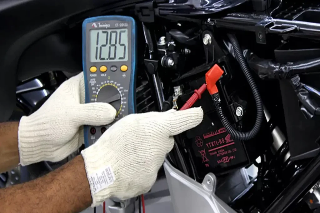 Teste de voltagem de bateria de moto com multímetro digital mostrando 12.85V.