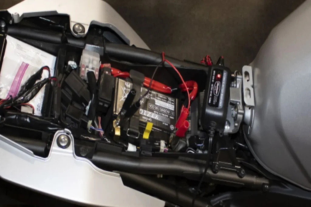 Bateria de moto sendo carregada com carregador conectado diretamente à motocicleta.