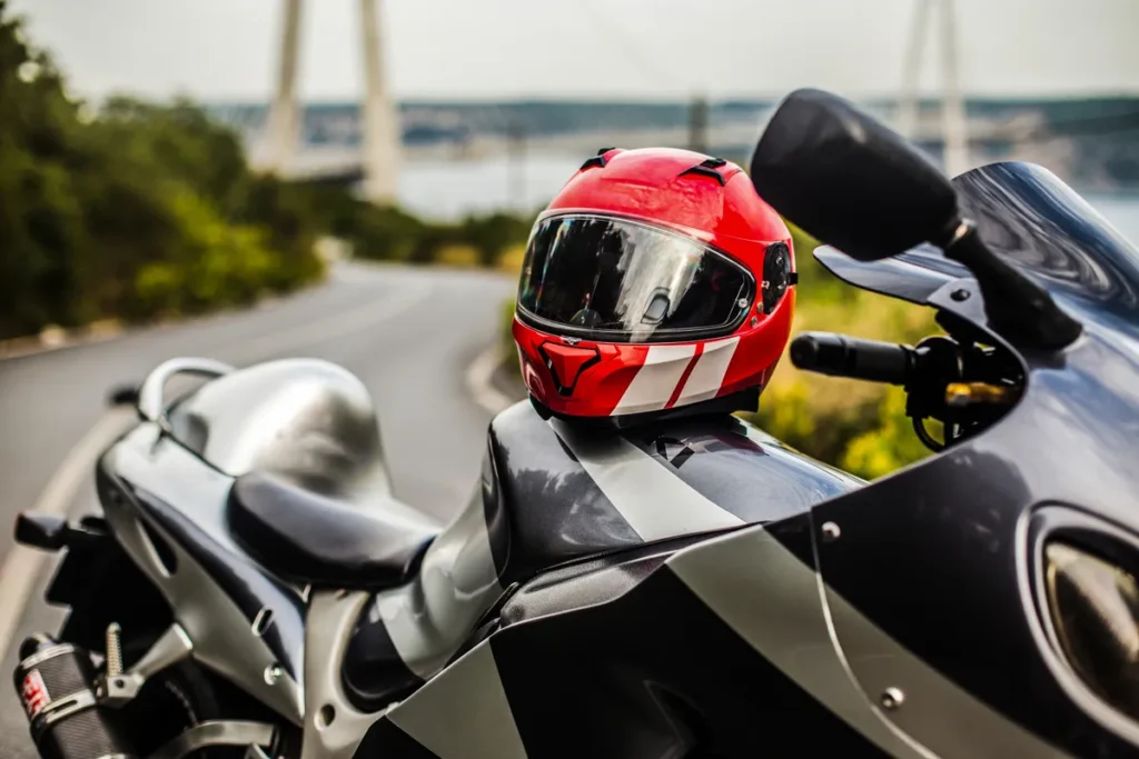 Capacete de motociclista vermelho sobre uma motocicleta esportiva estacionada em estrada sinuosa.