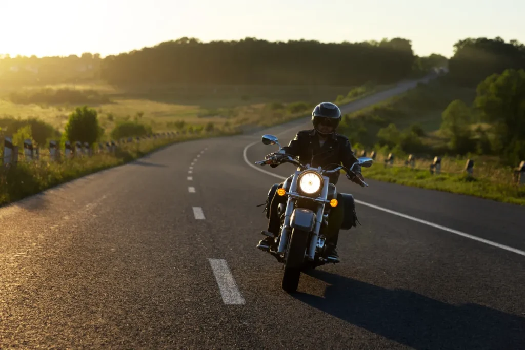 Motociclista pilotando em estrada deserta ao entardecer com capacete e jaqueta