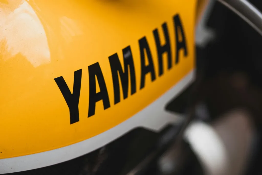 Close-up de tanque de motocicleta amarelo com o logotipo “YAMAHA” em letras pretas.