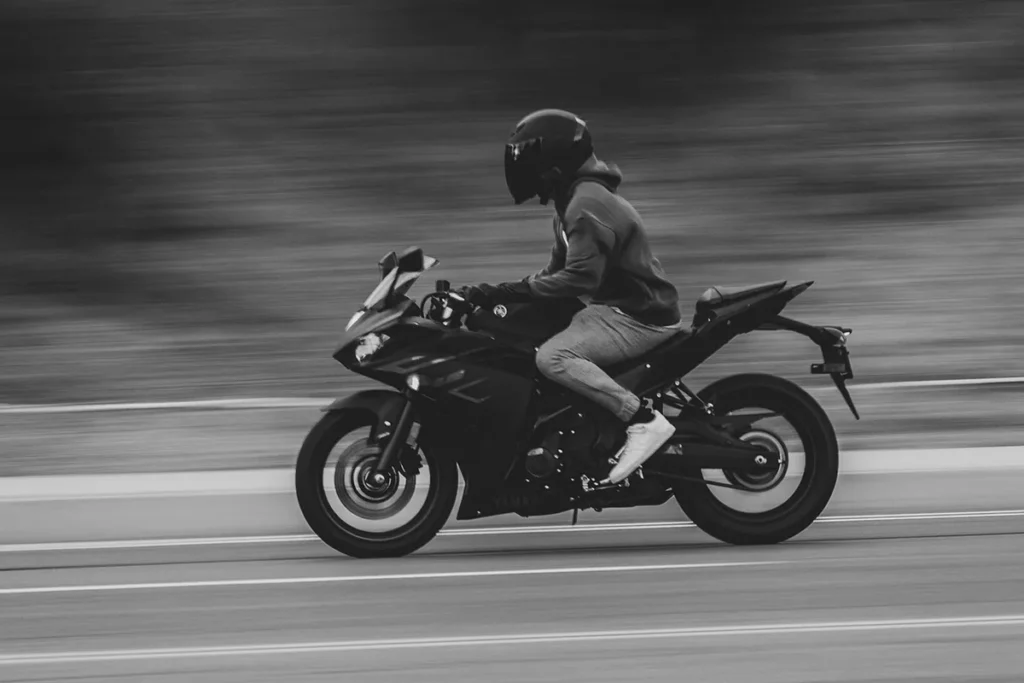 Motociclista usando capacete e jaqueta em uma moto esportiva em movimento capturada em preto e branco.