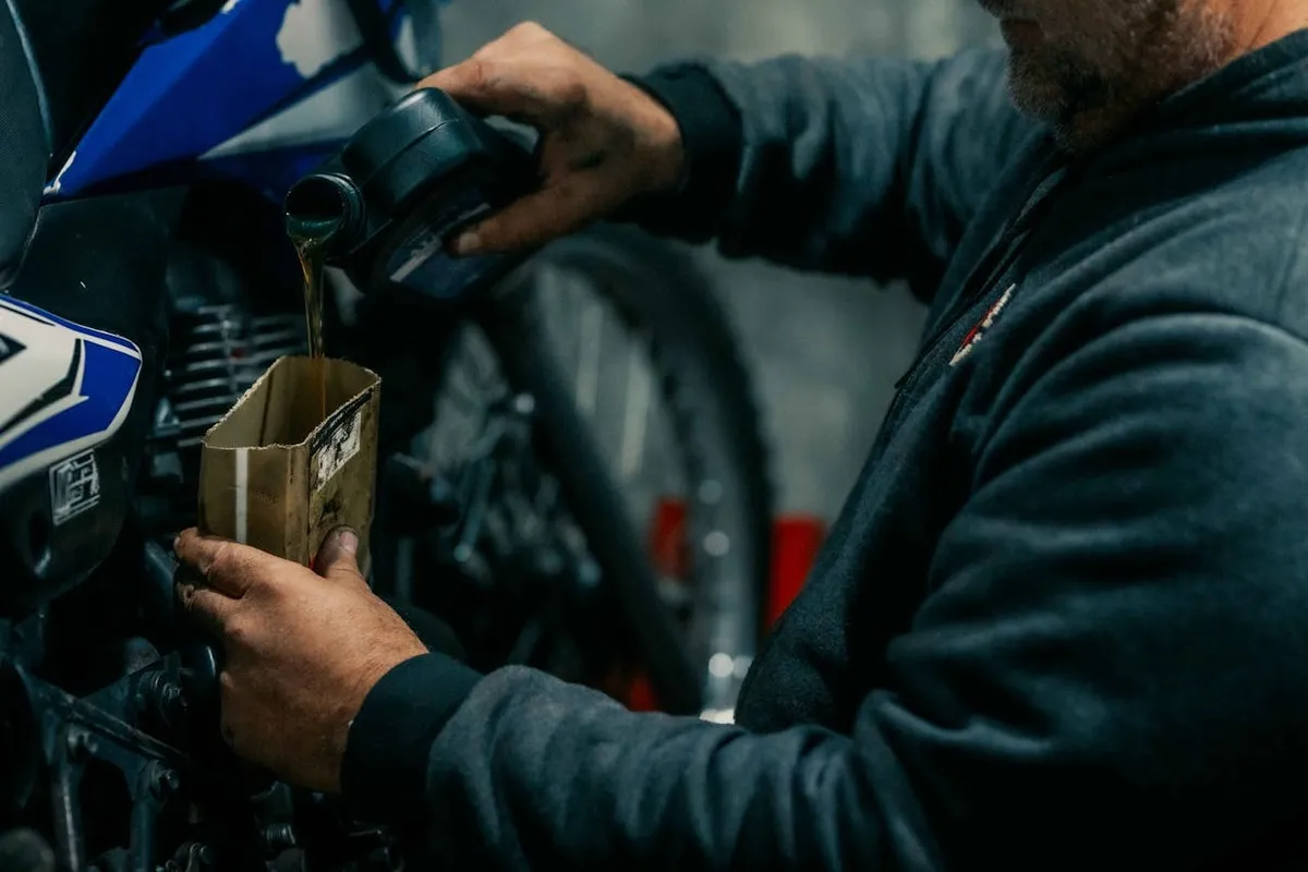 Mecânico derramando óleo em uma moto, simbolizando a manutenção geral que inclui a verificação do fluido de freio moto.