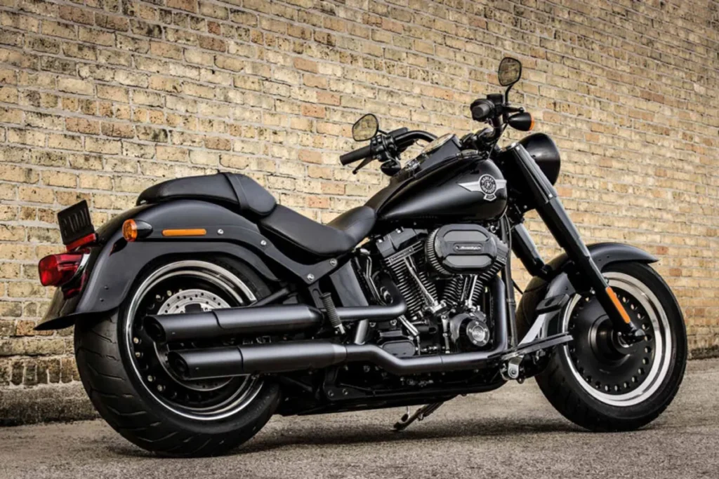 Moto Harley-Davidson preta modelo clássico, estacionada diante de parede de tijolos, exibindo design robusto e acabamento premium.