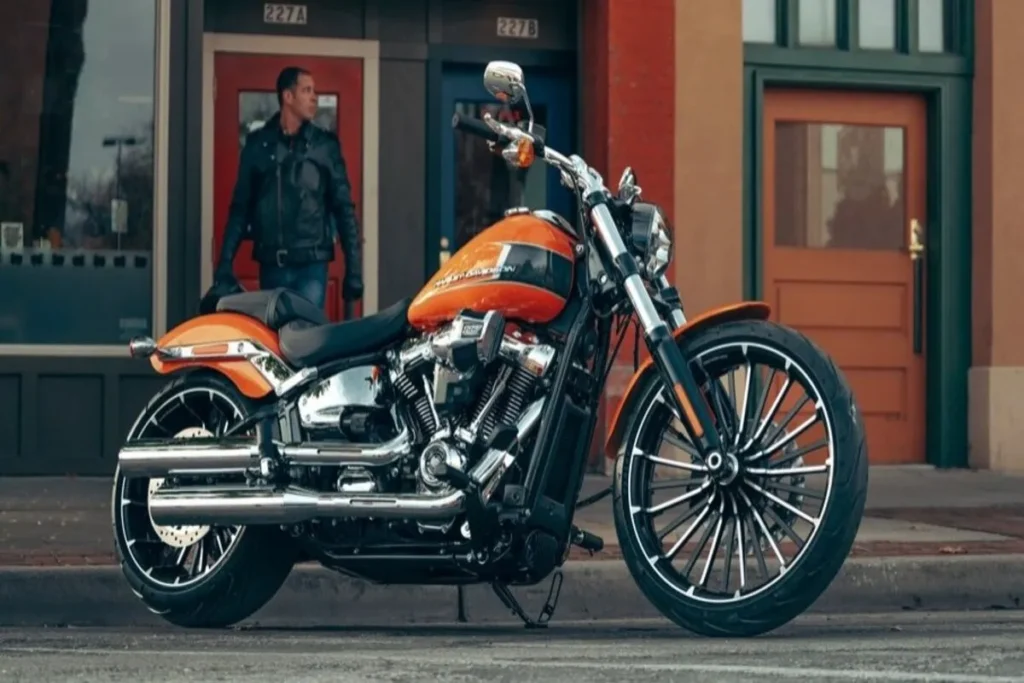 Moto Harley-Davidson laranja customizada, estacionada em rua urbana, destacando rodas raiadas e acabamento cromado.