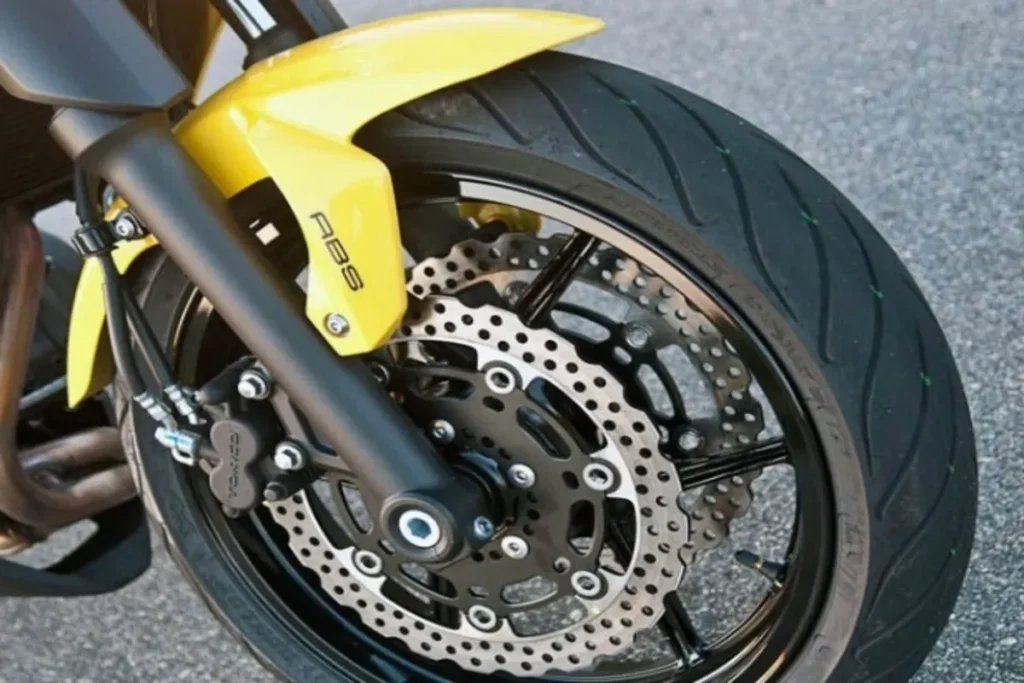 Roda dianteira de motocicleta com freio ABS, destacando o disco de freio duplo e o para-lama amarelo.